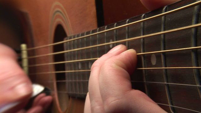 Detailed view of fingers skillfully playing acoustic guitar. This can be used in music tutorials, education scenarios, promotional materials for music schools, or blog posts about music techniques.