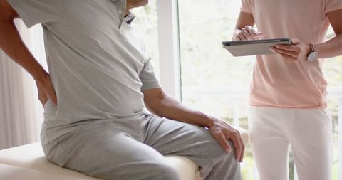 Senior Man Discussing Back Pain with Physiotherapist Using Tablet