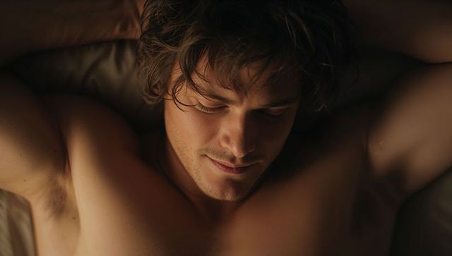 Reclining young man resting in warm low light intimate bare chest portrait stubble tousled hair