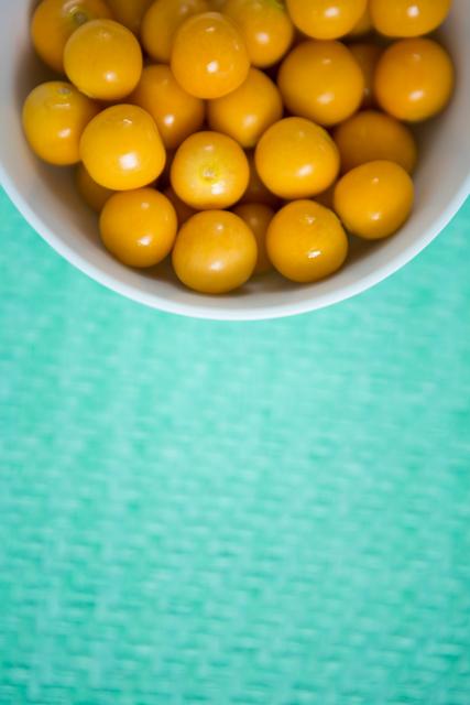 This image showcases a close-up view of fresh yellow cherries in a white bowl against a green background. Ideal for use in food blogs, healthy eating articles, summer fruit promotions, and organic produce advertisements.