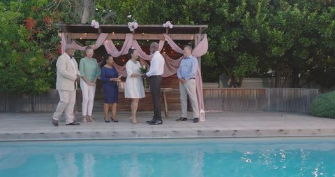 Senior Diverse Couple Exchanging Vows beside Pool with Friends