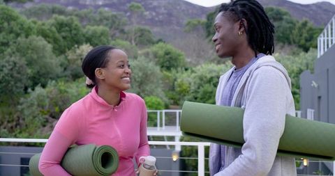 African American couple holding yoga mats on balcony smiling before outdoor workout