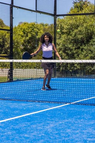 African american woman playing paddle tennis on vibrant blue outdoor court during sunny training