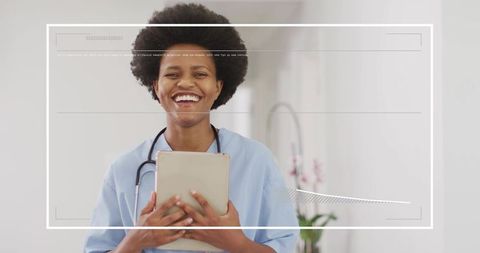 Smiling nurse holding tablet in modern hospital corridor wearing light blue scrubs