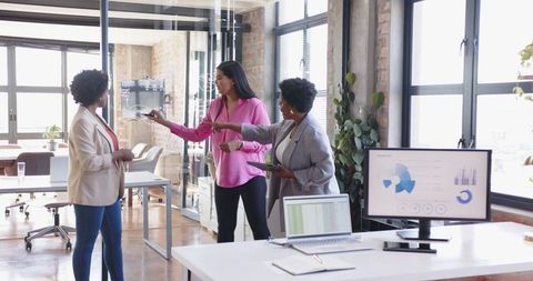 Diverse female team analyzing digital charts in modern office