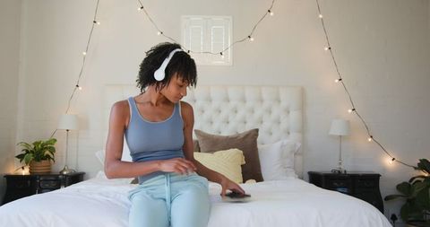 Young Woman Wearing Headphones Relaxing on Cozy Bedroom Bed