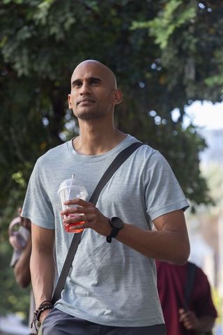 Thoughtful african american man holding iced drink walking with crossbody bag and smartwatch