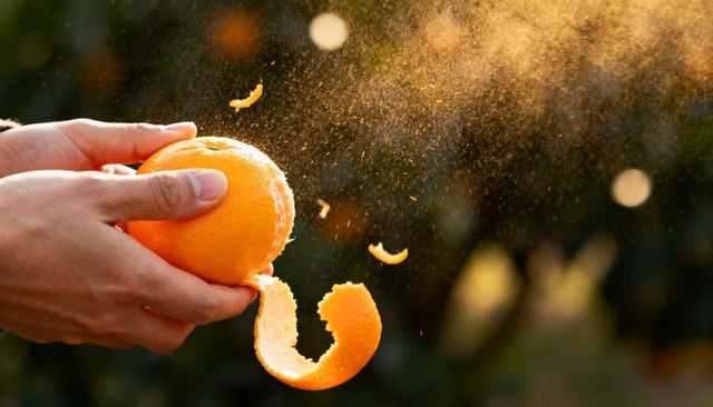 Peeling orange with backlit zest spray and long curled peel in golden sunlight