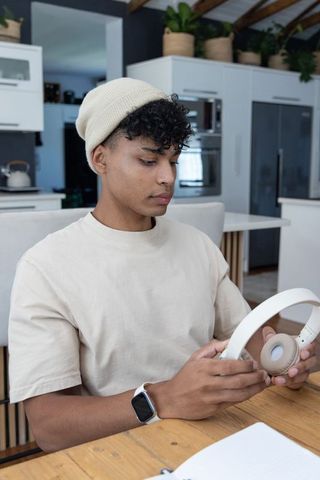 Young african american man sitting at wooden table inspecting wireless headphones