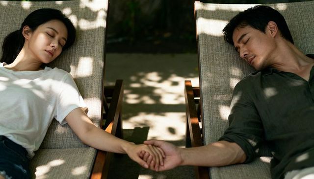 Reclining couple holding hands on sunlit lounge chairs with dappled garden shadows