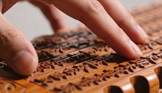 Fingertips tracing carved wooden blocks with raised symbols texture macro tactile craft closeup