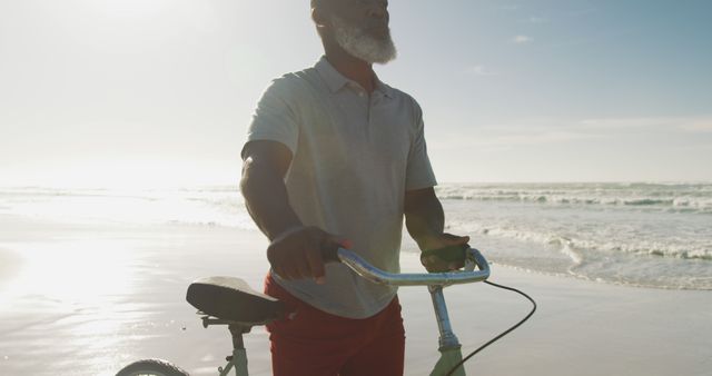 Senior african american man walking with a bicycle at the beach. healthy outdoor leisure time by the sea.