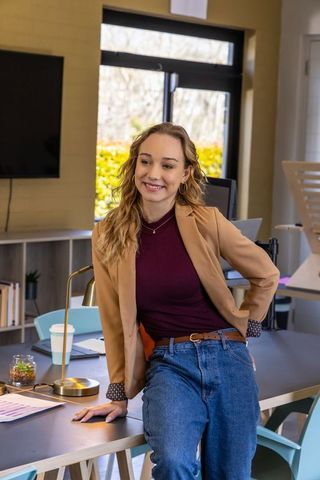 Young professional leaning on desk in modern office, smiling and relaxed
