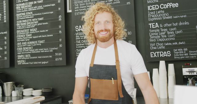 Portrait of happy caucasian male barista using tablet behind counter in cafe. Local business owner and hospitality concept.