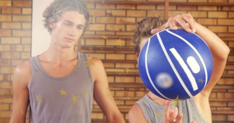 Teen coaching younger boy with blue basketball in indoor gym brick wall bars bonding skills