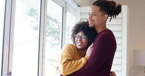 African American Couple Embracing by Window Wearing Cozy Mustard and Maroon Knit Sweaters