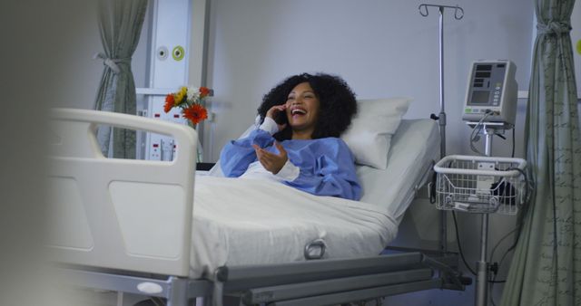 African american female patient lying on hospital bed talking on smartphone and smiling. medicine, health and healthcare services.