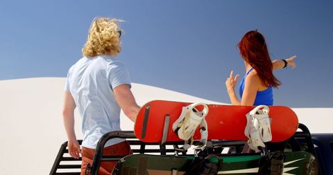 Couple Preparing for Sandboarding Adventure in Sunny Desert
