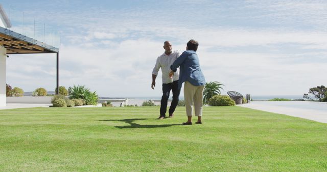 Man and woman embracing on a well-maintained lawn, with a modern house and the sea in the background on a sunny day. It conveys a sense of togetherness and contentment. Ideal for use in advertisements related to family, relationships, home living, or real estate. Suitable for lifestyle and vacation promotions highlighting serene and joyful moments.