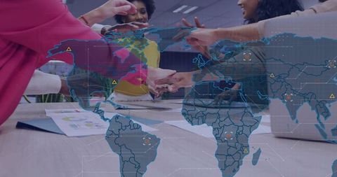 Multicultural team joining hands over desk with global map overlay for teamwork