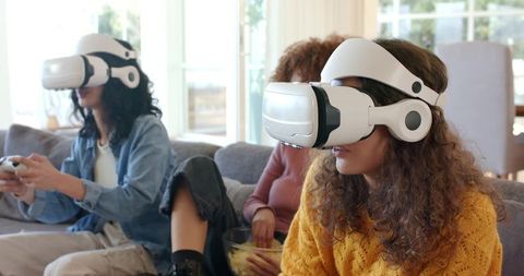 Young women enjoying virtual reality gaming on couch sharing popcorn in bright living room