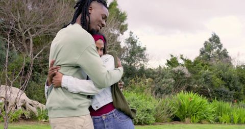 Diverse couple embracing in lush garden, woman wearing headscarf, man in sweatshirt