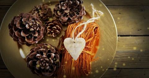 Rustic christmas table centerpiece with pine cones, raffia heart ornament and warm bokeh