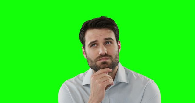 A man in a light dress shirt resting his hand on his chin, looking thoughtful with a neutral green screen background. Perfect for projects requiring custom backdrop insertions, business English training materials, advertisements focusing on decision-making processes, or educational materials exploring problem-solving concepts.