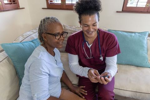 Male nurse showing glucometer to senior african american woman during home health visit