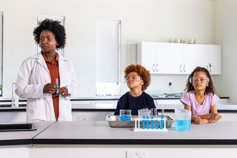 Female science instructor guiding elementary students hands-on test tube experiment