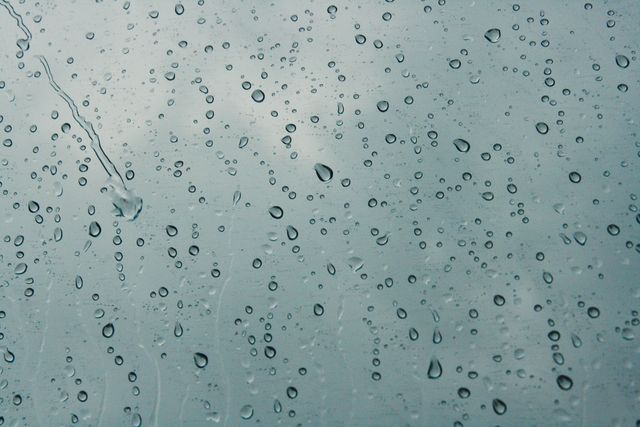 Close-up view of raindrops sticking to a glass window. Ideal for use in projects related to nature, weather patterns, or moody, melancholic atmospheres. Can be used as a background or in articles and presentations discussing rainy weather or the natural beauty of raindrops.
