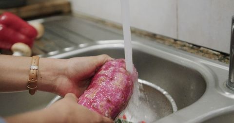 Hands washing fresh purple meat in kitchen sink for safe cooking