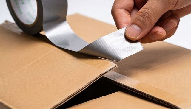 Hand sealing corrugated cardboard box with silver duct tape for shipping, packing and repair