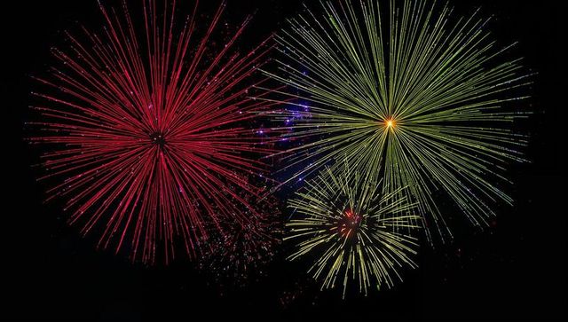 Vivid fireworks bursting red chrysanthemum and lime-yellow starbursts lighting midnight sky