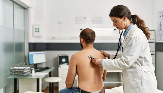 Female doctor listening to male patient with stethoscope during routine clinic checkup