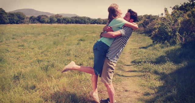 This image captures a joyous moment between a young couple embracing in a grassy countryside field. Ideal for use in advertisements, relationship blogs, travel websites, or any content that celebrates love and romance in natural settings. The vibrant outdoor setting makes it perfect for themes related to nature, happiness, and youthful energy.