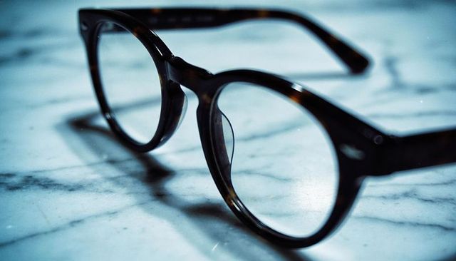 Round tortoiseshell glasses resting on marble countertop, clear lenses reflecting dust
