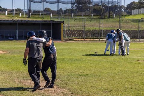 Senior teammates walking arm-in-arm on sunny baseball field showing camaraderie and teamwork