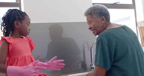 African american grandmother teaching granddaughter washing dishes together at kitchen sink
