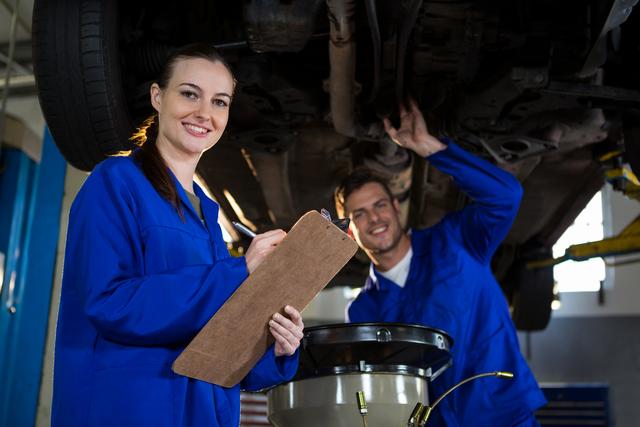 Mechanics preparing a check list while his colleague examining a car engine in the background