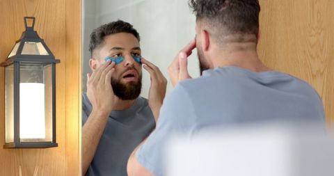 man applying blue under-eye gel patches in bathroom - Download Free Stock Images Pikwizard.com