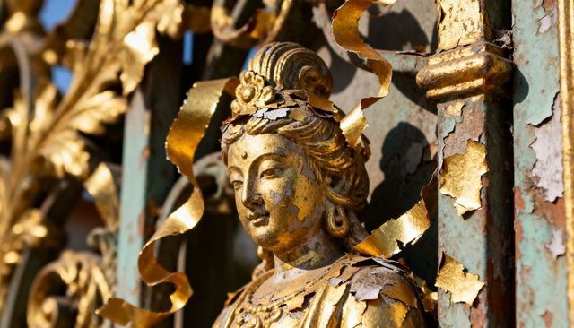 Gilded ornamental bust with peeling gold leaf and patina on ornate gate catching sunlight