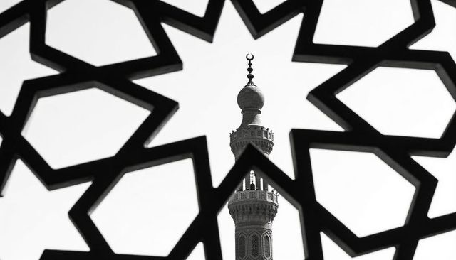 Framing ornate mosque minaret through star-shaped geometric lattice, monochrome silhouette