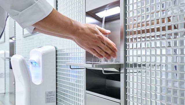 Hands washing under sensor faucet in modern restroom with stainless sink and mosaic tile