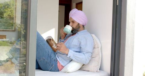 Man in Turban Relaxing at Home by Window with Book and Coffee