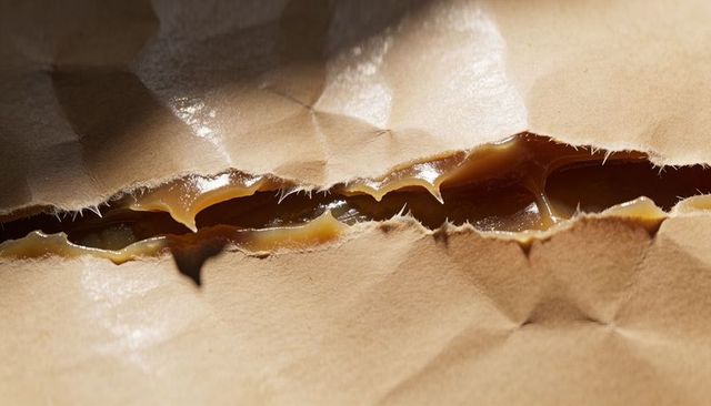 Revealing torn kraft paper with glossy caramel filling close-up texture and sticky tear