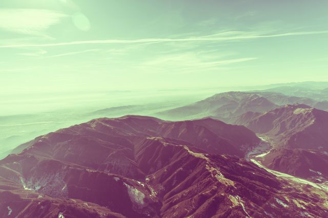 This image presents a stunning aerial perspective of a mountain range with a vintage filter, emphasizing the beauty and vastness of nature. The clear sky and the foggy distance add to the serene and timeless feel of the view. Ideal for use in travel blogs, adventure-themed websites, or as inspirational wallpaper. Perfect for illustrating concepts of natural beauty, outdoor activities, and scenic landscapes.