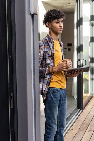 Young Hispanic Man Relaxing with Coffee and Tablet on Modern Residential Deck