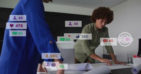 Leaning colleagues reviewing blueprints with social media overlays in boardroom