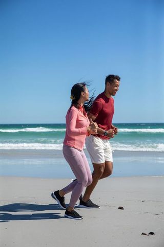 Diverse Couple Jogging Along Sandy Beach Coastline in Activewear